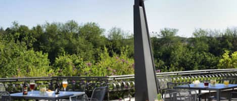 Un espace extérieur aménagé pour les repas, avec des tables et des chaises, un grand parasol et un barbecue.