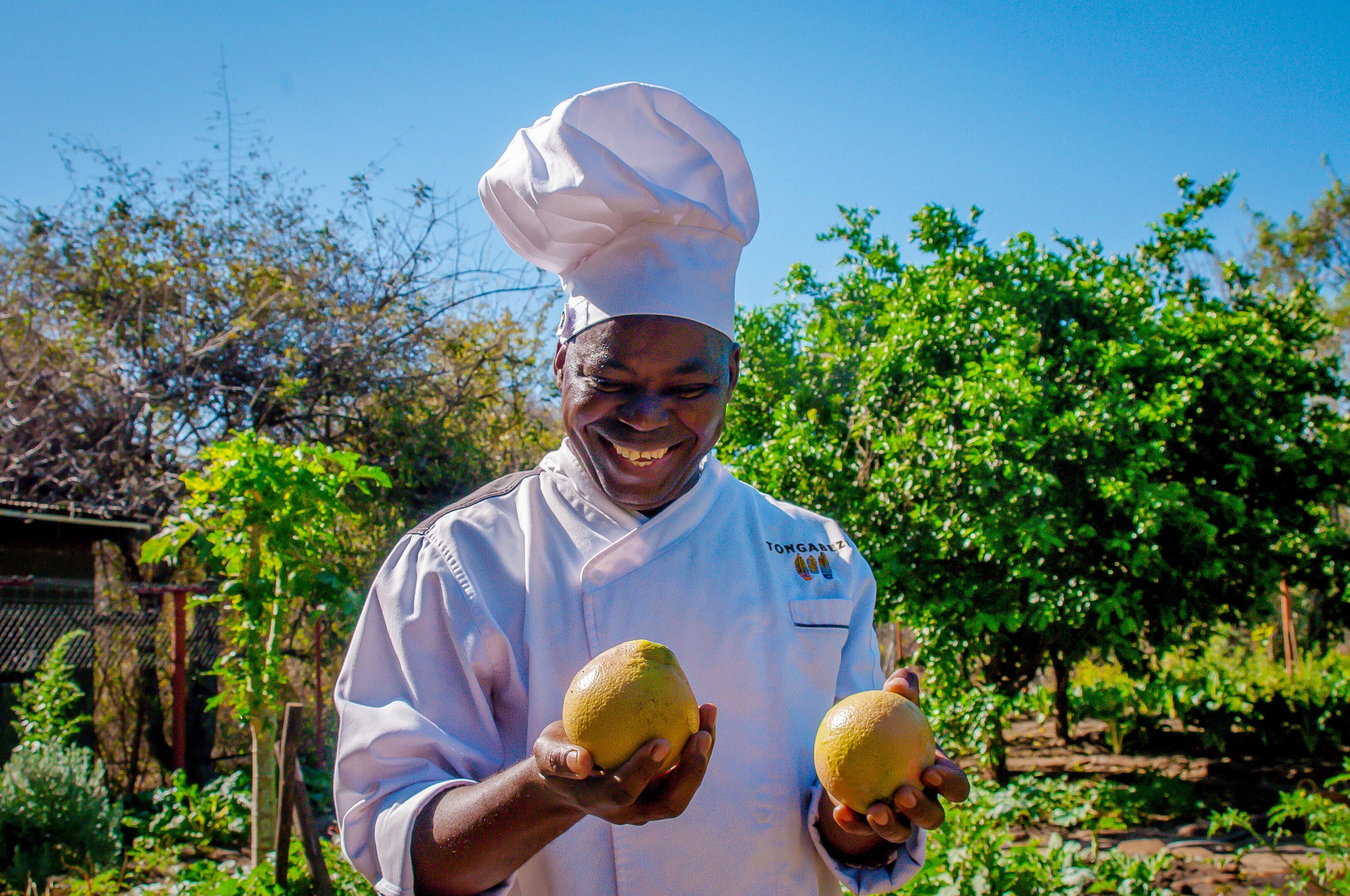 Un chef sostiene dos frutas en un jardín.