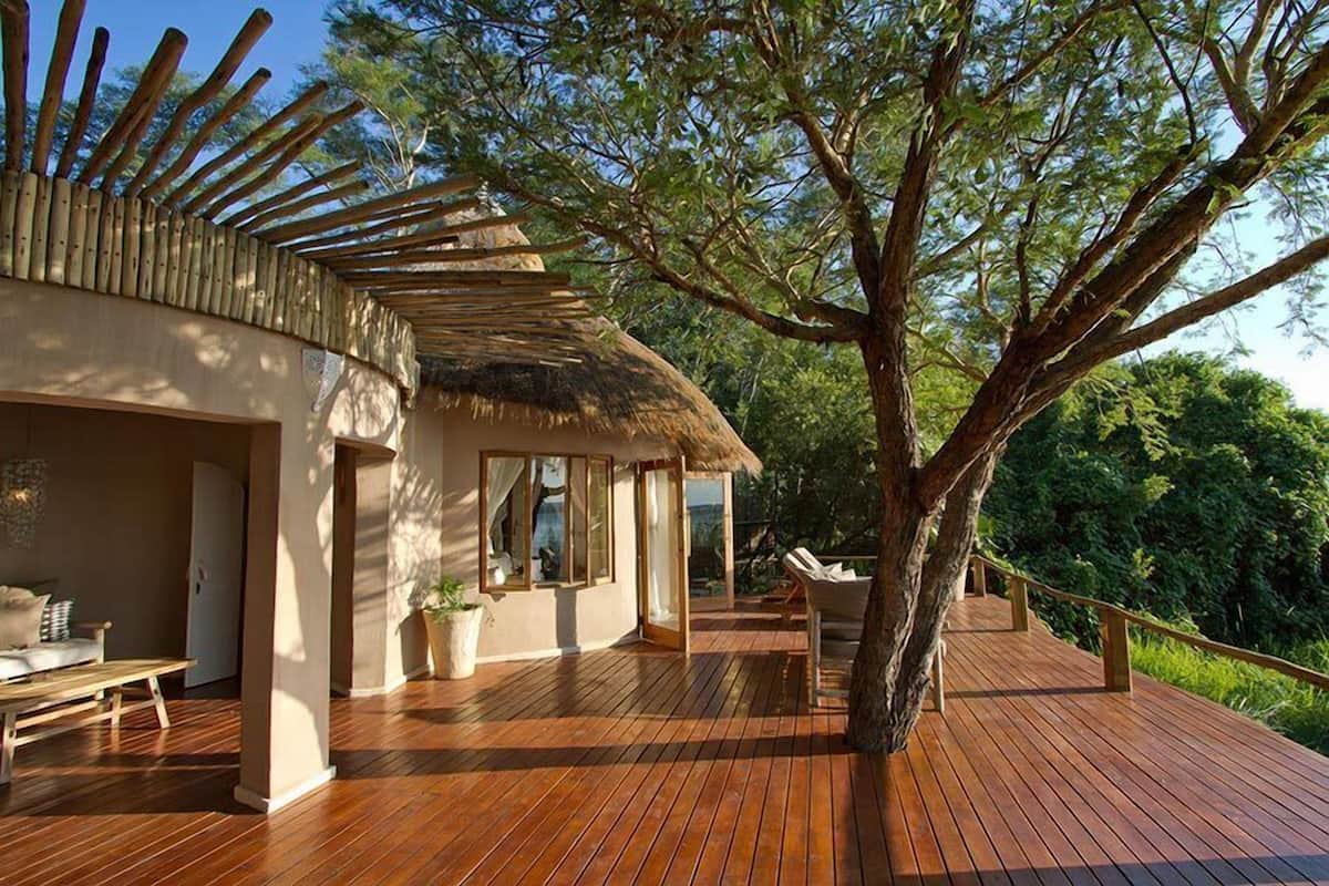 A wooden deck with a thatched-roof structure, a lounge area, and a view of the surrounding greenery.