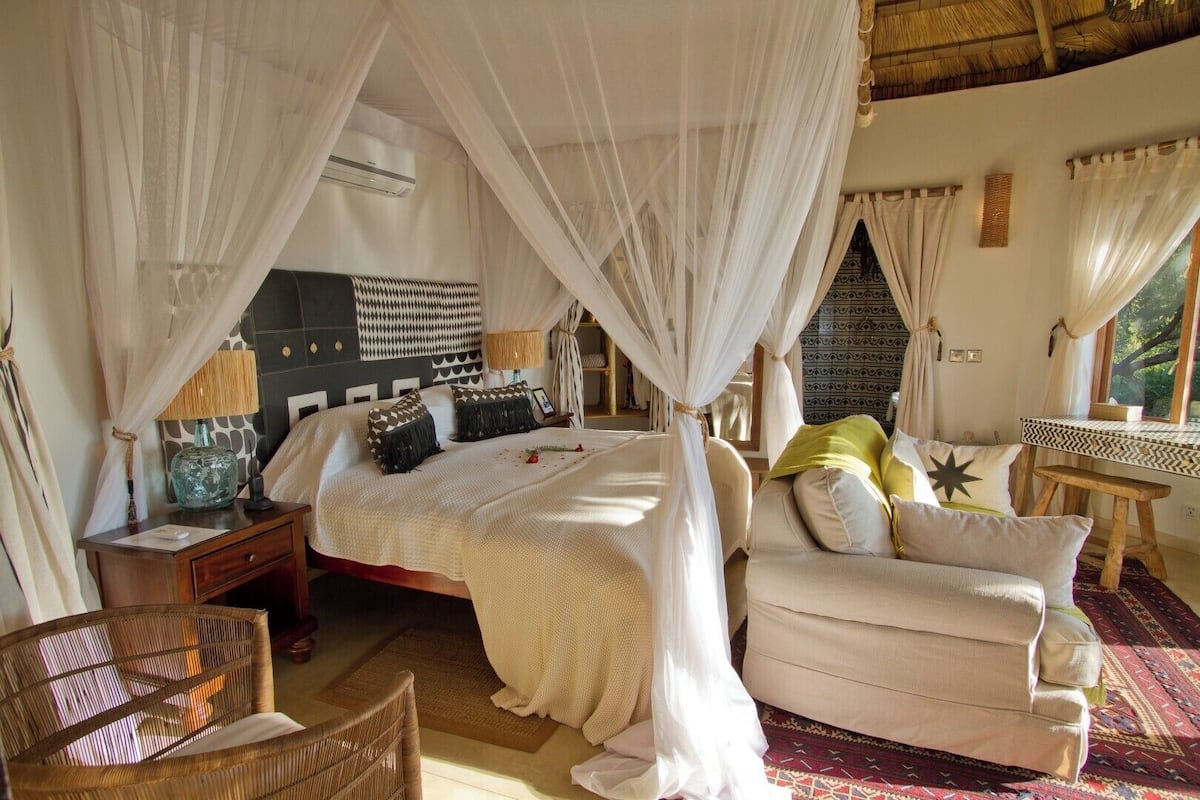 A bedroom with a canopy bed, a sofa, a wooden table, and a wicker chair.