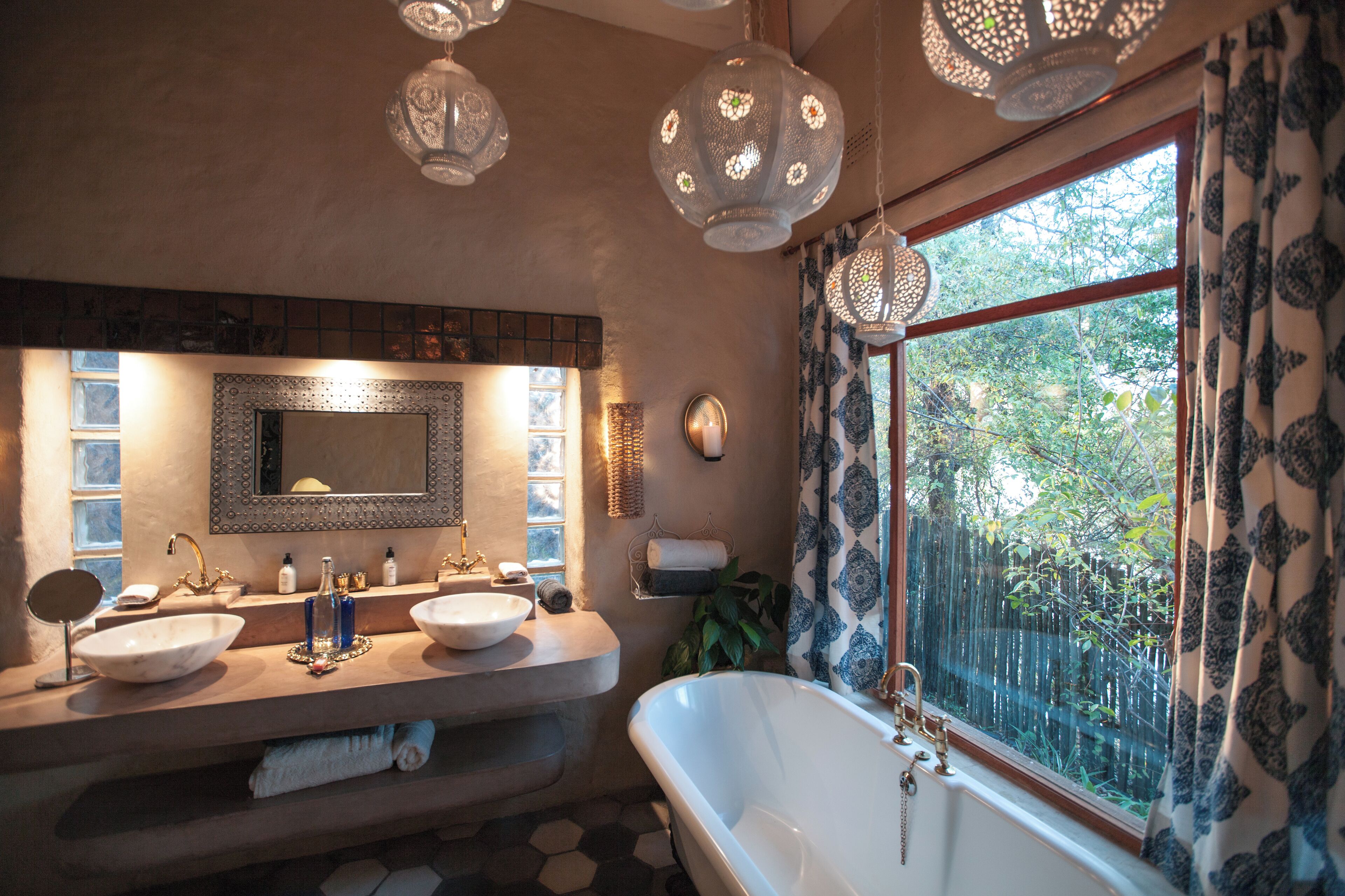 A bathroom with two sinks, a large mirror, a bathtub, and a window with patterned curtains.