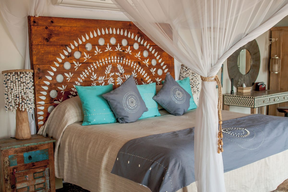 A bed with a canopy, decorative pillows, a wooden headboard, and a bedside table with a lamp.