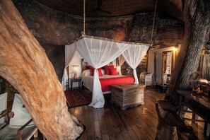 A rustic bedroom with a canopy bed, wooden furniture, and a large tree trunk in the corner.