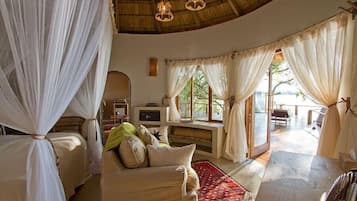 A cozy room with a bed, a sofa, and a table. There are curtains and a window with a view.