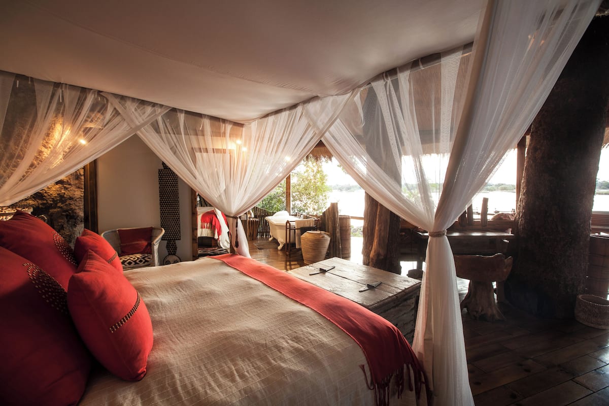 A bed with a canopy, a red throw blanket, and a view of an outdoor area with a table and chairs.