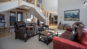 A spacious living area with a high ceiling, a staircase, leather furniture, and a large painting. - Dreamcatcher Bed and Breakfast (Victor)