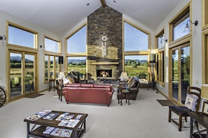 A spacious living room with a fireplace, leather sofas, and large windows offering a view of the countryside.