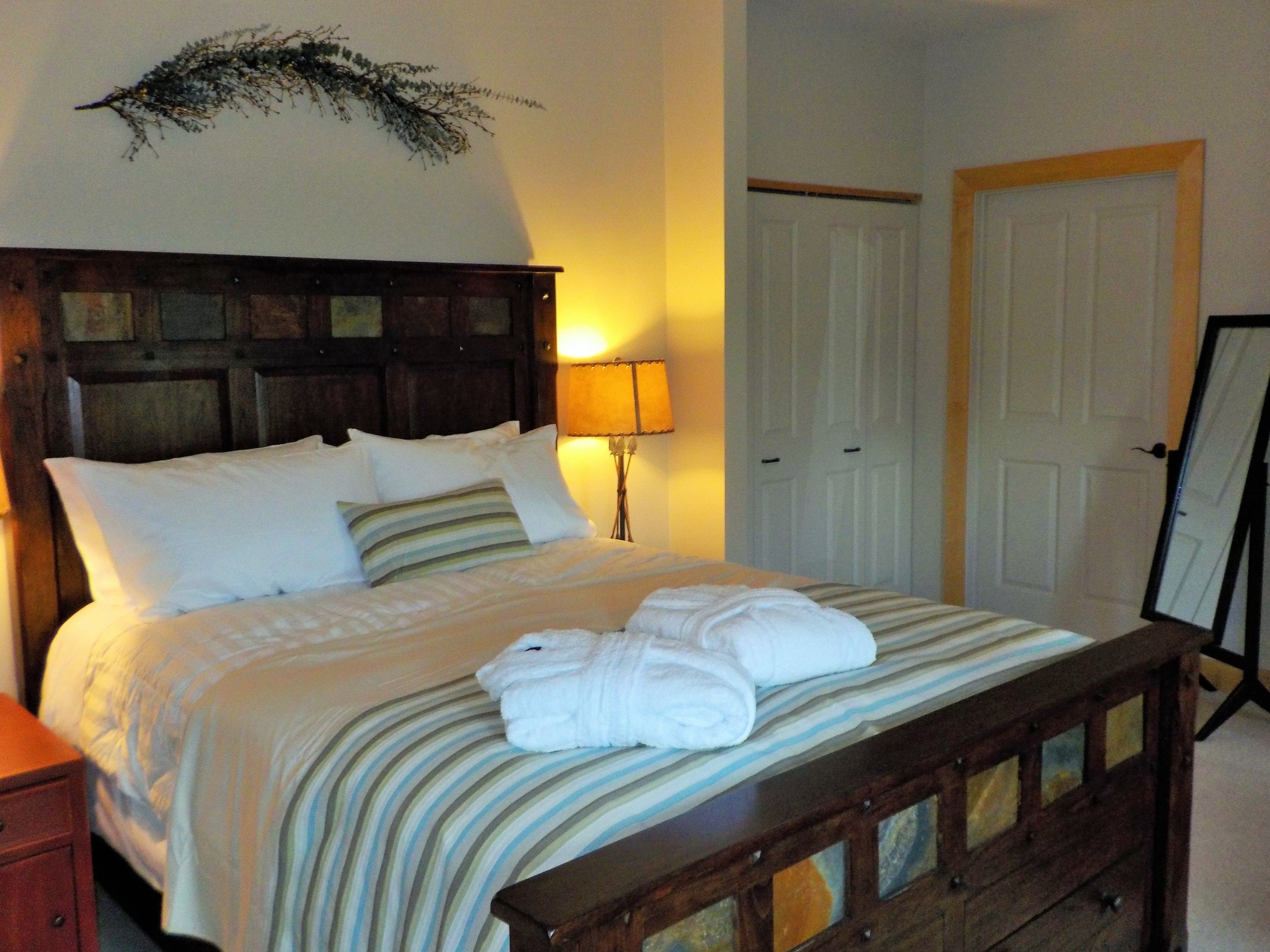 A neatly made bed with white linens and striped bedding, a bedside lamp, and a wooden headboard.