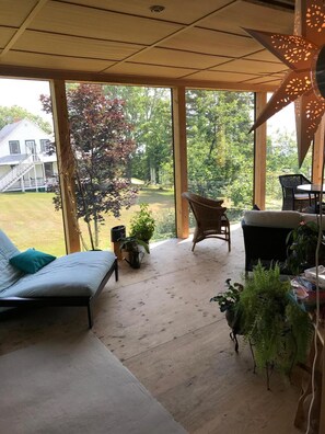 A covered patio with a sofa, chairs, and potted plants. - Auberge A La Chouenne (La Malbaie)