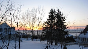 Un quartier résidentiel avec des maisons, des arbres sans feuilles et un paysage enneigé au coucher du soleil.