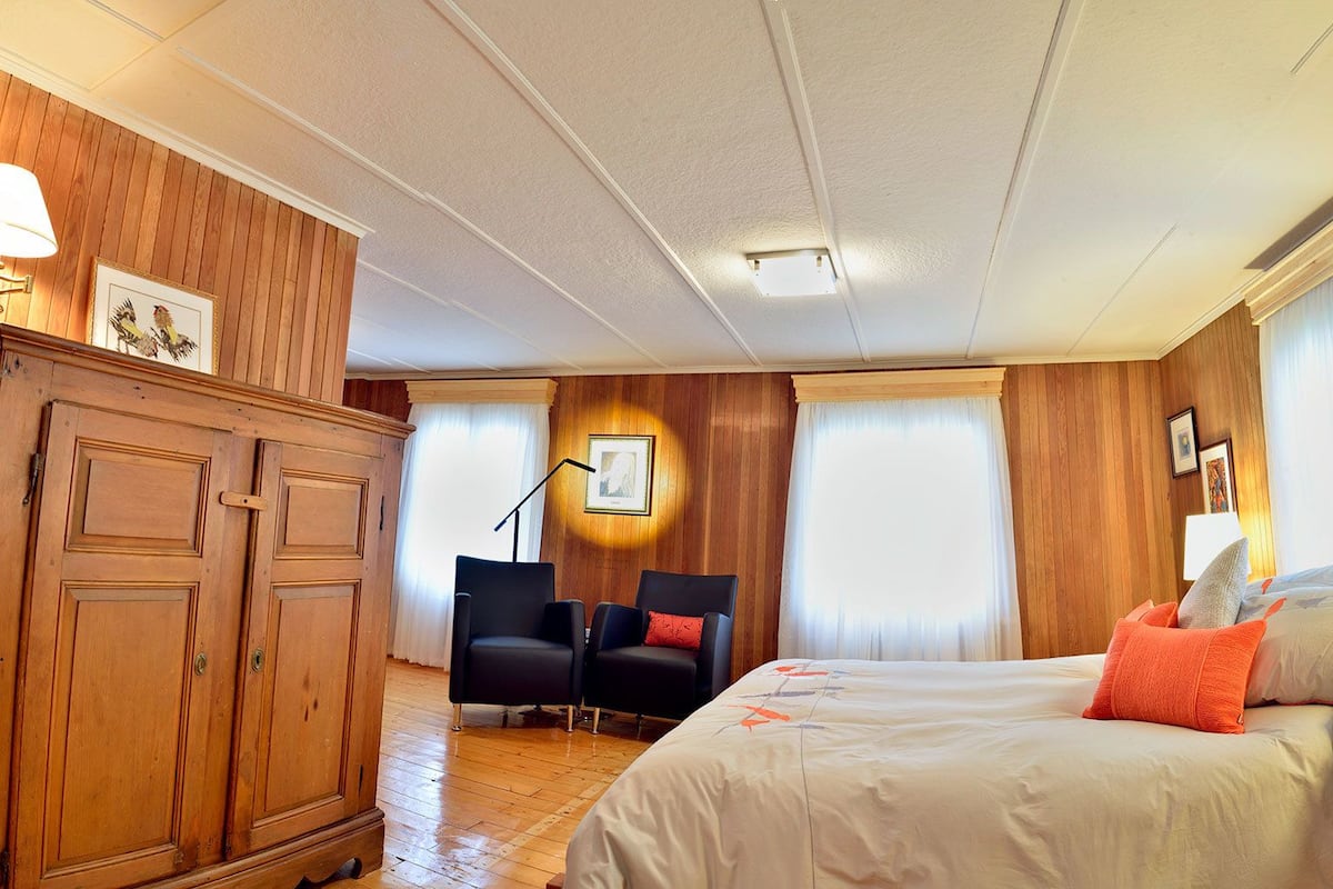 Una habitación de hotel con un armario de madera, una cama con almohadas naranjas, un escritorio con lámpara y una silla.