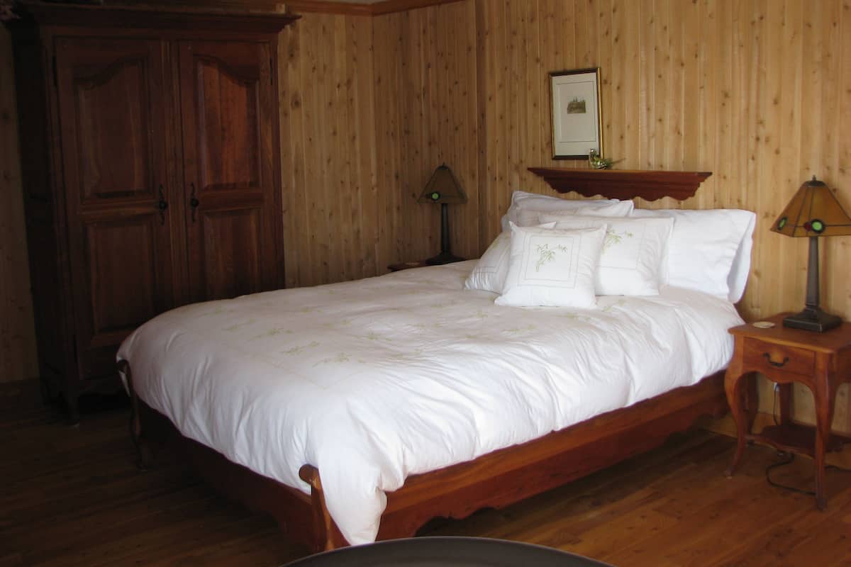 Un dormitorio con paneles de madera, una cama grande, dos mesitas de noche y un armario.
