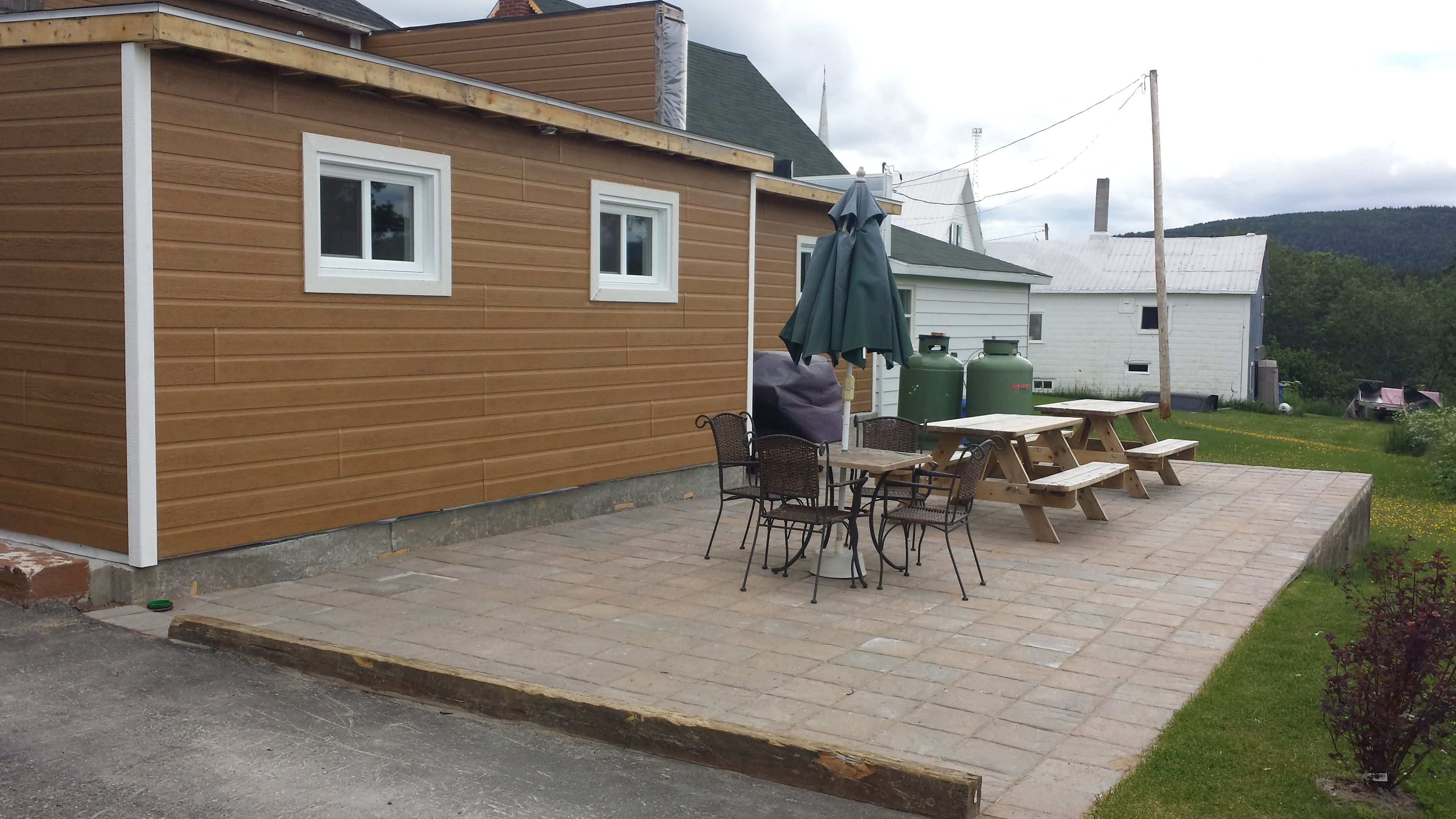A patio with wooden tables and chairs, a covered umbrella, and a green gas cylinder.