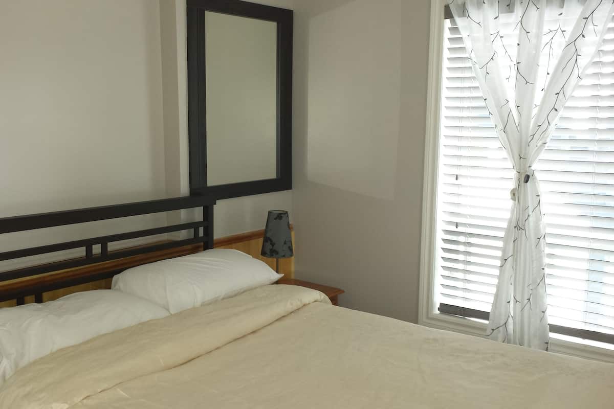 A bed with a wooden headboard, a bedside lamp, and a window with blinds.