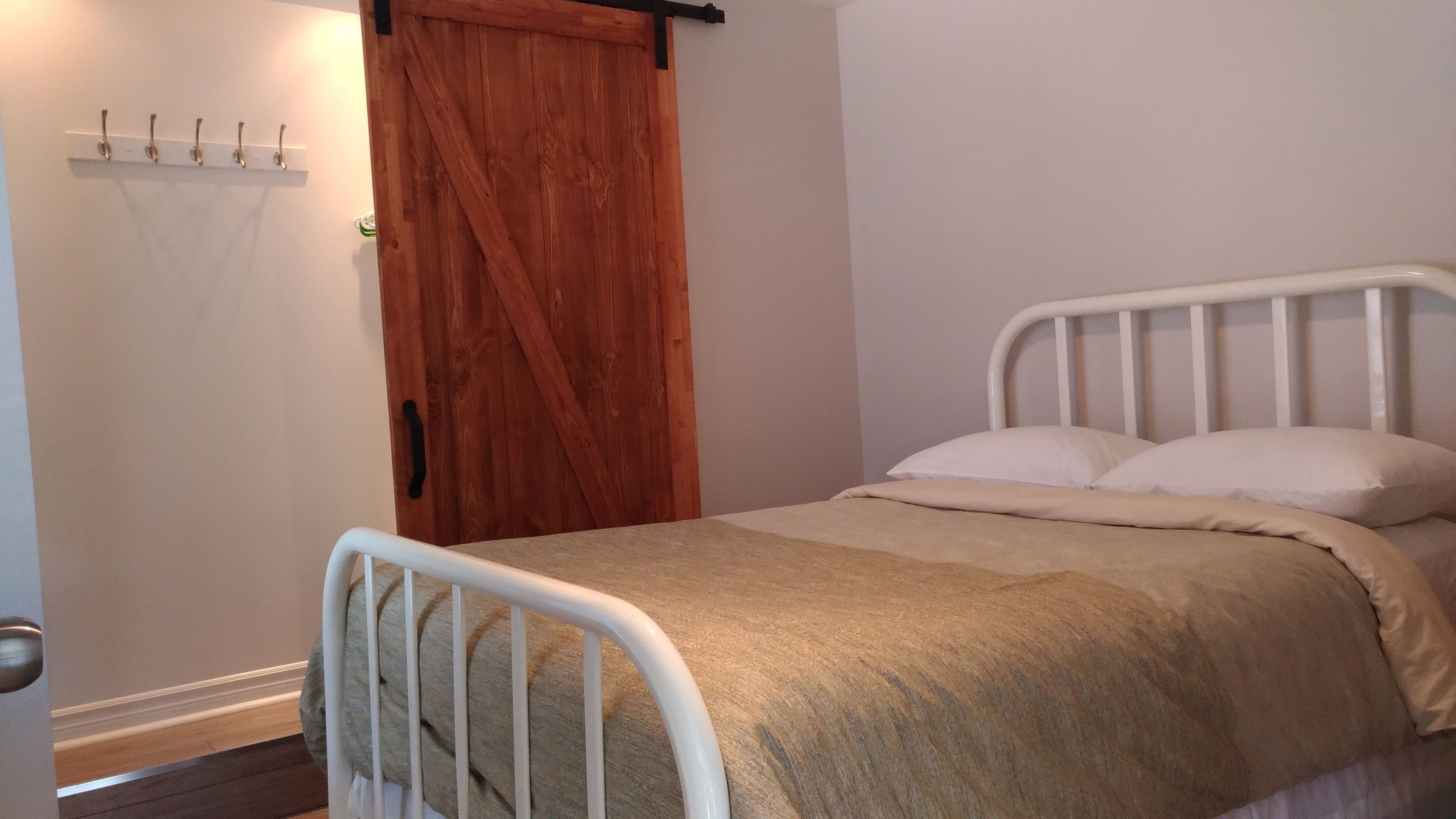 A bedroom with a wooden door, a white metal bed frame, and a beige bedspread.