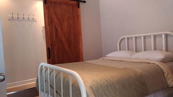 A bedroom with a wooden door, a white metal bed frame, and a beige bedspread.
