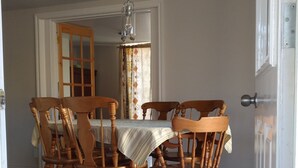 A dining area with a round table and six wooden chairs, a hanging light fixture, and a door leading to another room. - Les Appartements de la Bergeronnette (Les Bergeronnes)