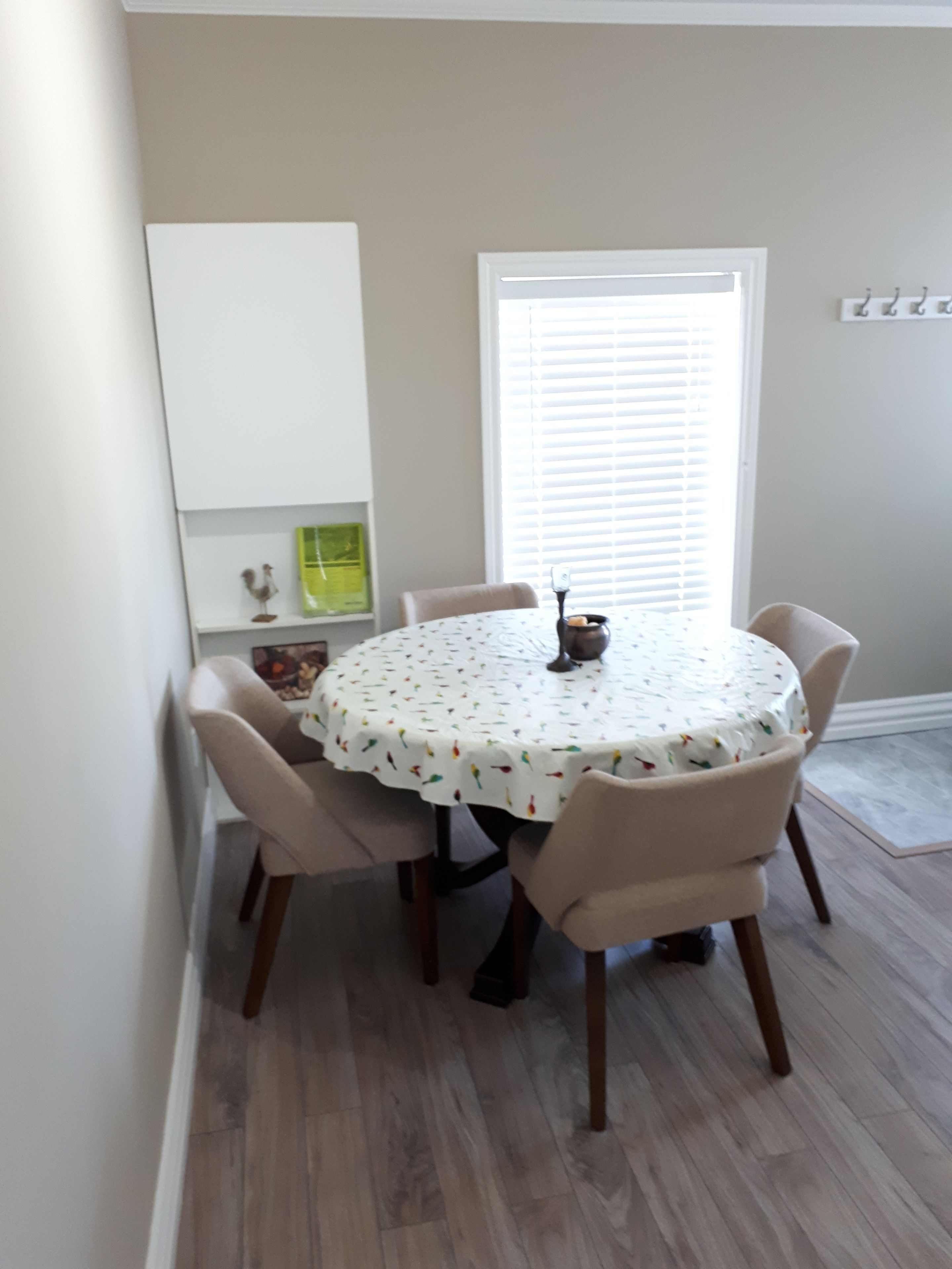A dining area with a round table covered by a white tablecloth with a pattern, surrounded by four chairs.