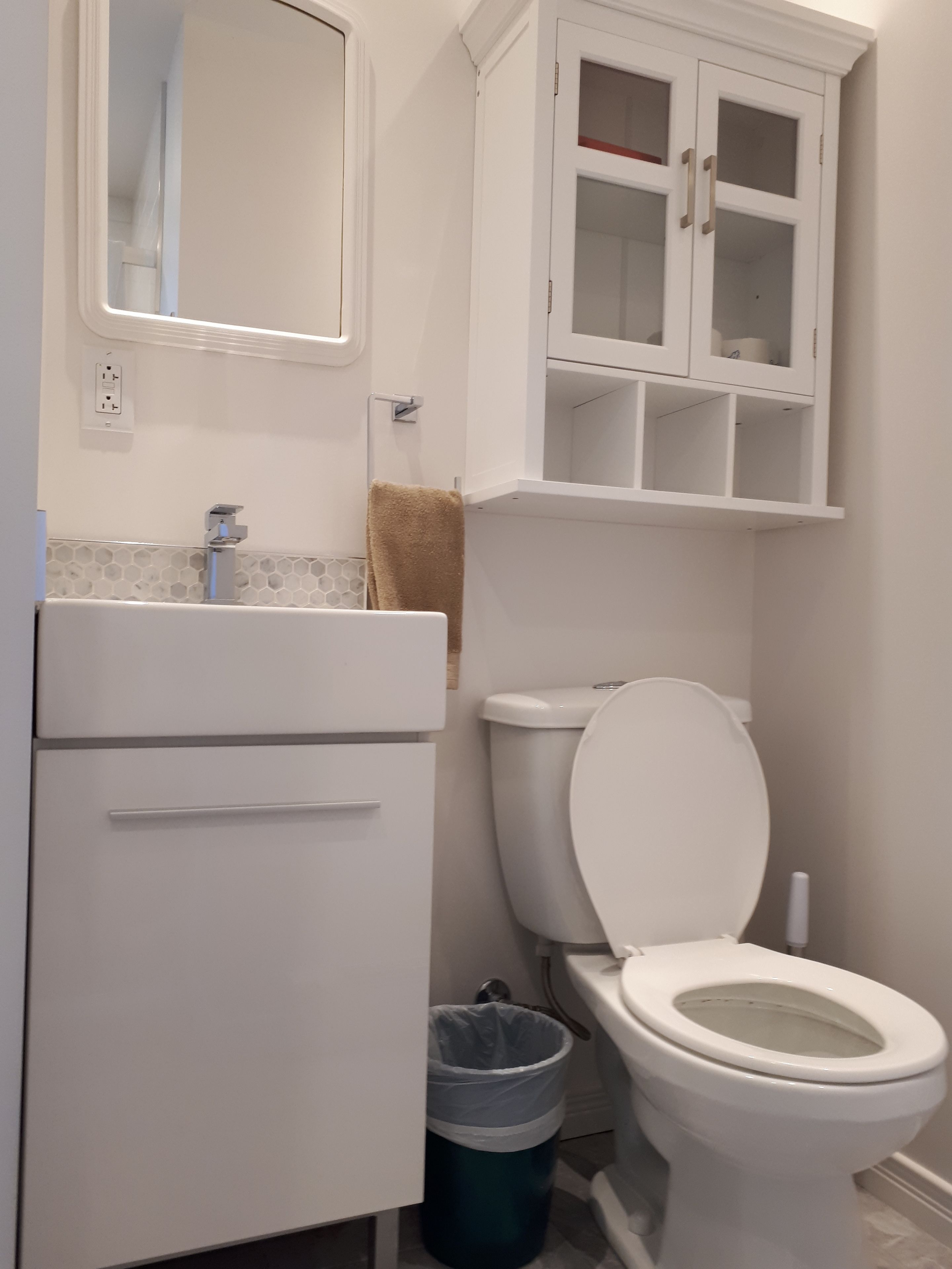 Een badkamer met toilet, wastafel, spiegel en kast.