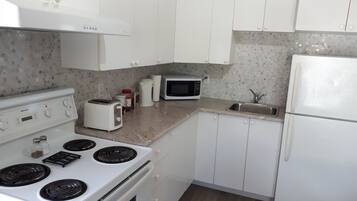 A kitchen with white cabinets, a stove, a microwave, a toaster, and a sink.