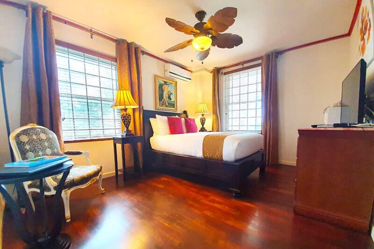 Een hotelkamer met een bed, een bureau, een stoel, een plafondventilator en een televisie.