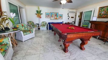 A room with a pool table, comfortable seating, and a ceiling fan.