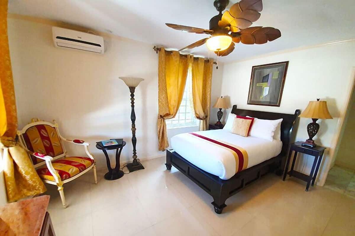 Een hotelkamer met een bed, een stoel, een vloerlamp, een bureau en een plafondventilator.
