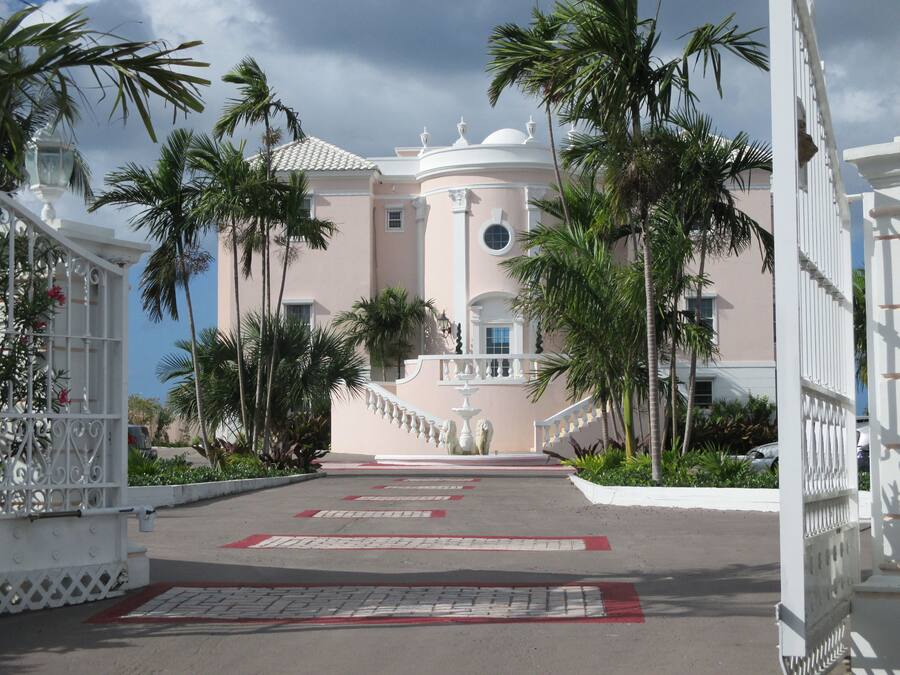 A grand building with a central staircase, surrounded by palm trees and a white fence.
