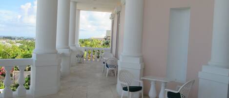 A covered outdoor area with white columns, a white table with chairs, and a view of greenery and buildings in the distance.