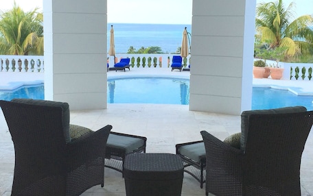 A pool area with lounge chairs and a view of the ocean.