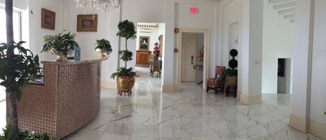 A spacious lobby with a marble floor, a reception desk, potted plants, and a chandelier.