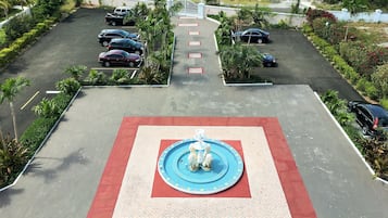 A parking lot with a fountain in the center, surrounded by greenery and palm trees.