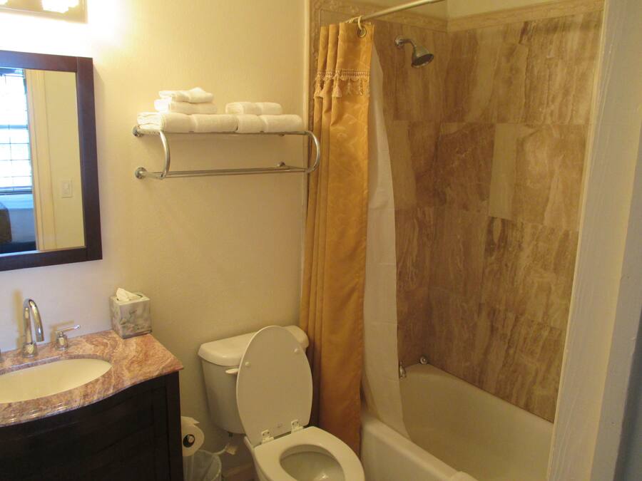 A bathroom with a toilet, sink, and bathtub. There is a towel rack with towels above the toilet.