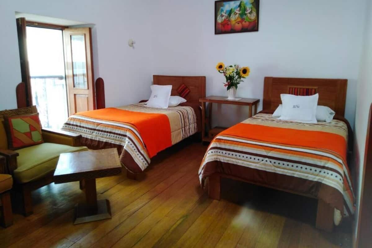 A room with two beds, a small table, a chair, and a window.