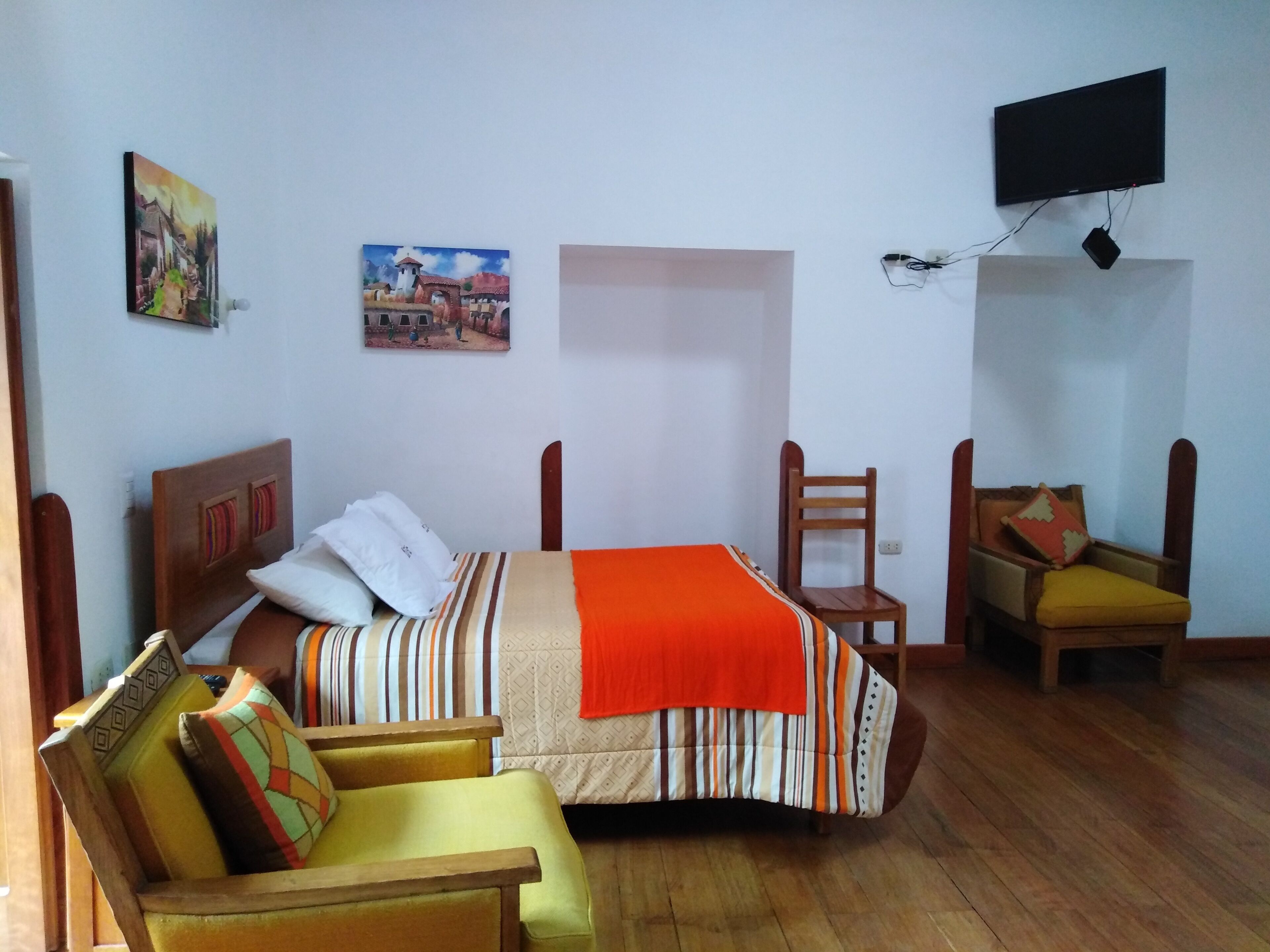 A room with a bed, a chair, a sofa, a TV, and two paintings on the wall.