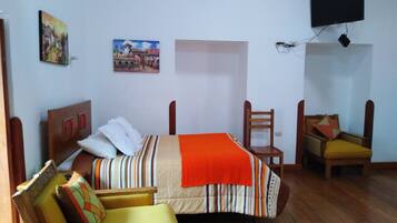 A room with a bed, a chair, a sofa, a TV, and two paintings on the wall.