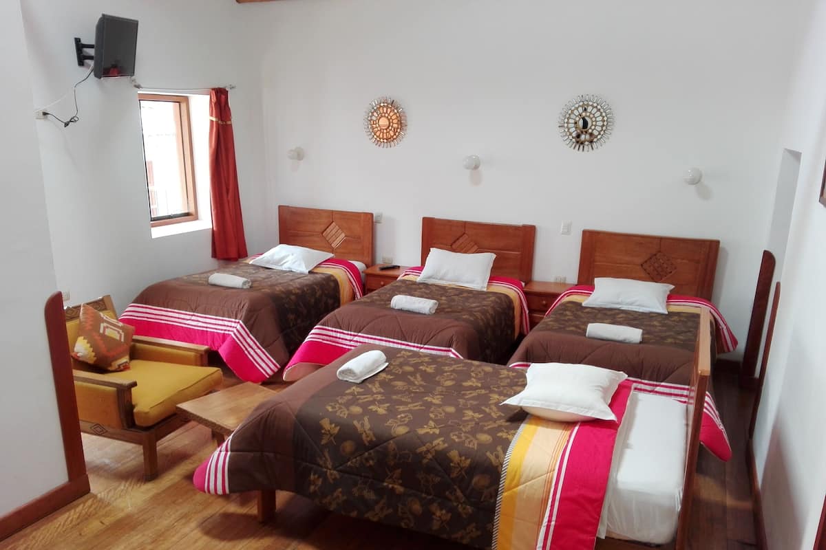 A hotel room with four beds, wooden flooring, a small desk, and a chair.