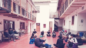 Un patio con un grupo de personas sentadas en círculo, bancos a lo largo de las paredes y una escalera que conduce a un nivel superior.