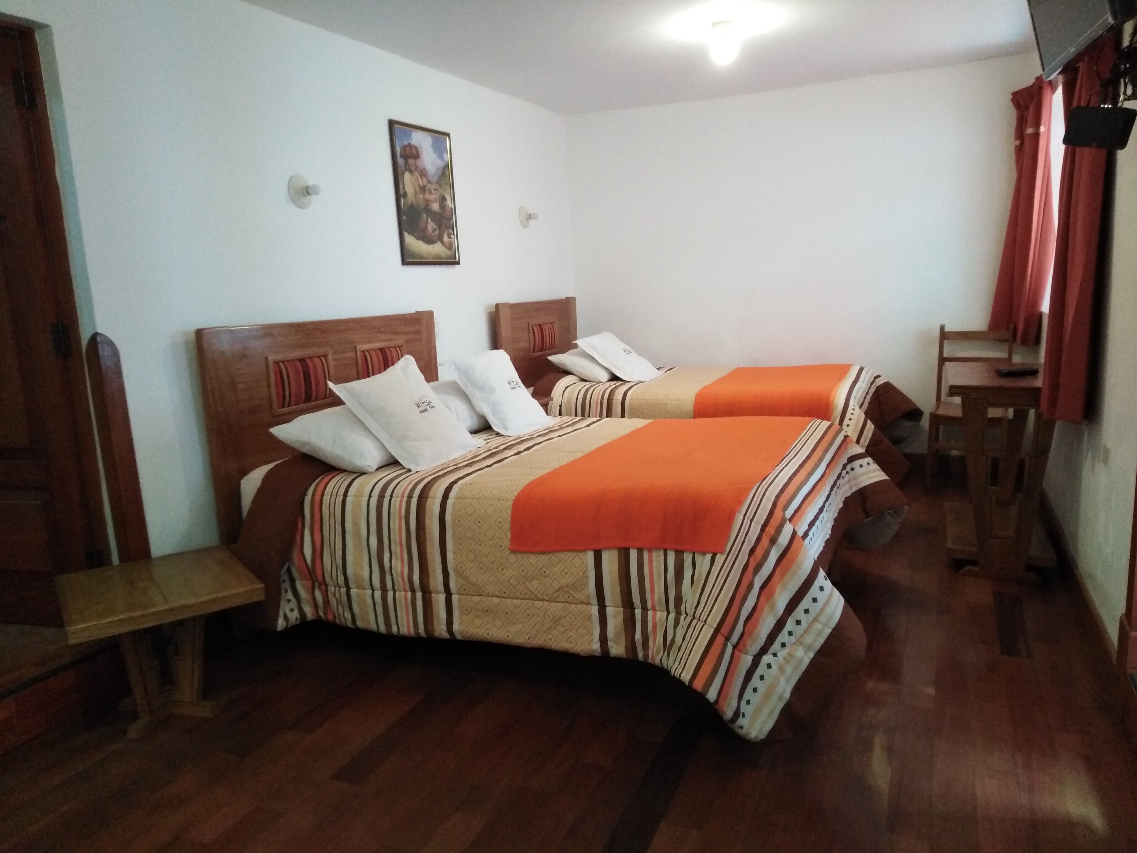 Una habitación con dos camas, cabeceros de madera, una mesita y un cuadro en la pared.