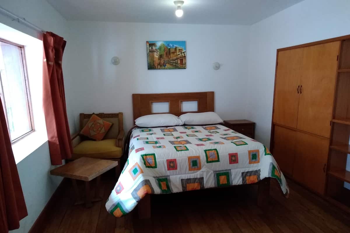 A bedroom with a wooden bed, a wooden nightstand, a wooden wardrobe, a window with curtains, and a painting on the wall.