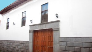 Un edificio con una puerta de madera grande, fachada blanca y suelo de baldosas.