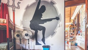 Quarto com um mural de uma pessoa tocando guitarra, decoração com tridente e um ventilador.