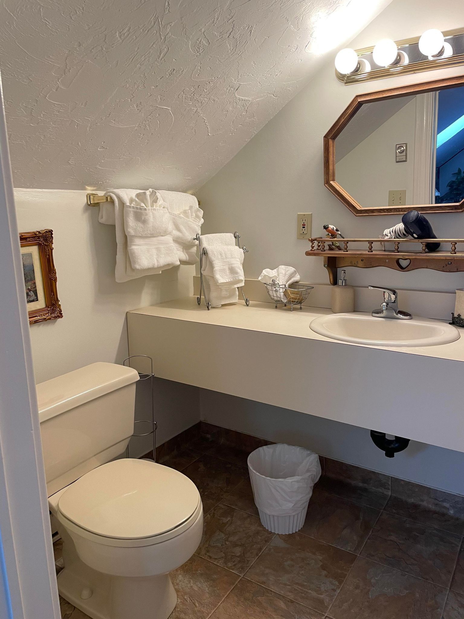 A bathroom with a toilet, sink, vanity, and a mirror with lights.