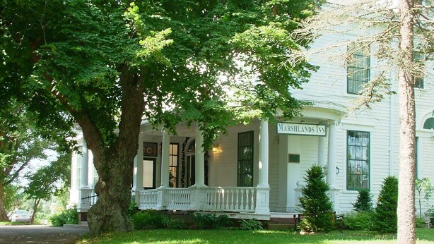 A two-story building with a porch and a sign that reads "Marshlands Inn." - Marshlands Inn (Sackville)
