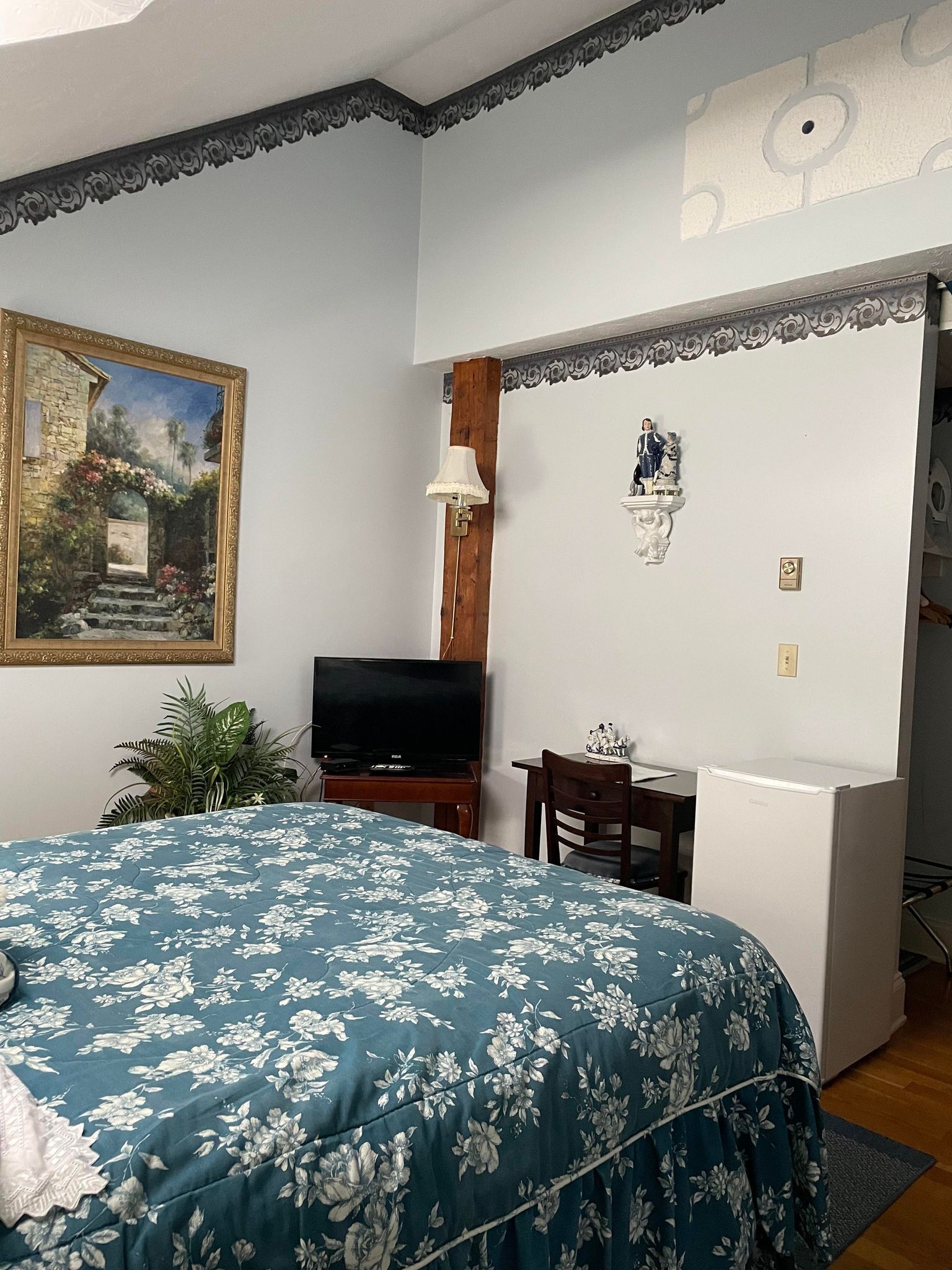 Un dormitorio con cama, televisor, escritorio y una pequeña estatua en la pared.