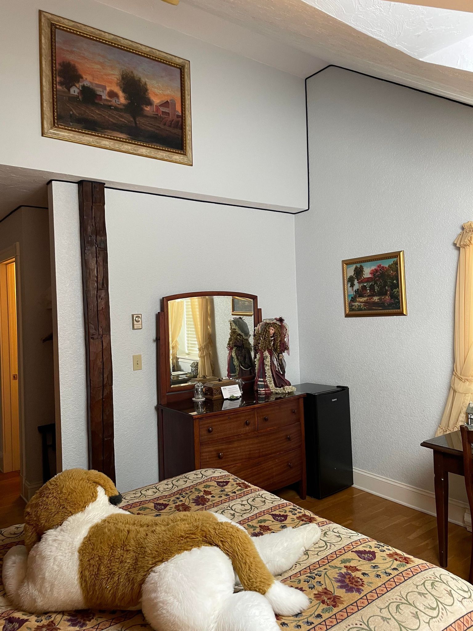 A bedroom with a bed, dresser, mirror, and two framed pictures on the wall.