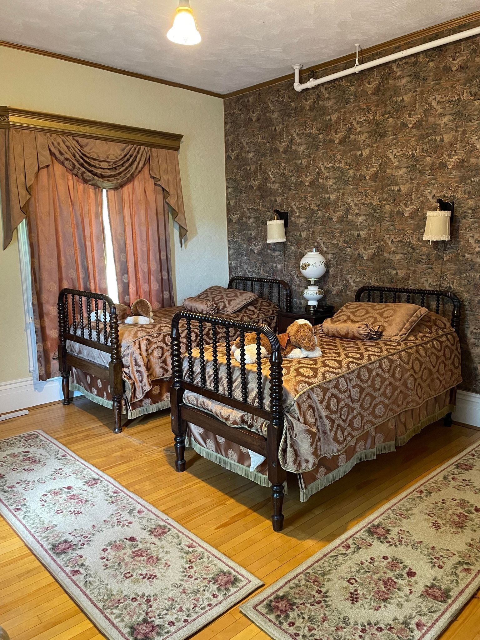 A bedroom with two wooden beds, a patterned rug, a decorative wall, and a window with curtains.