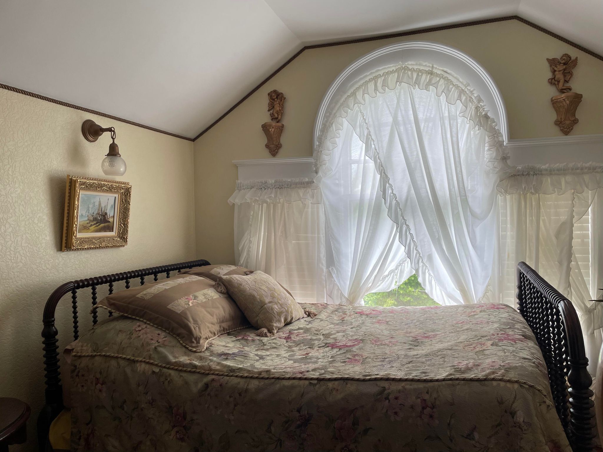 A bedroom with a bed, a picture frame, a window with sheer curtains, and decorative wall moldings.