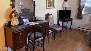 A room with a wooden desk, a chair, a television, a mirror, and a painting on the wall. - Marshlands Inn (Sackville)