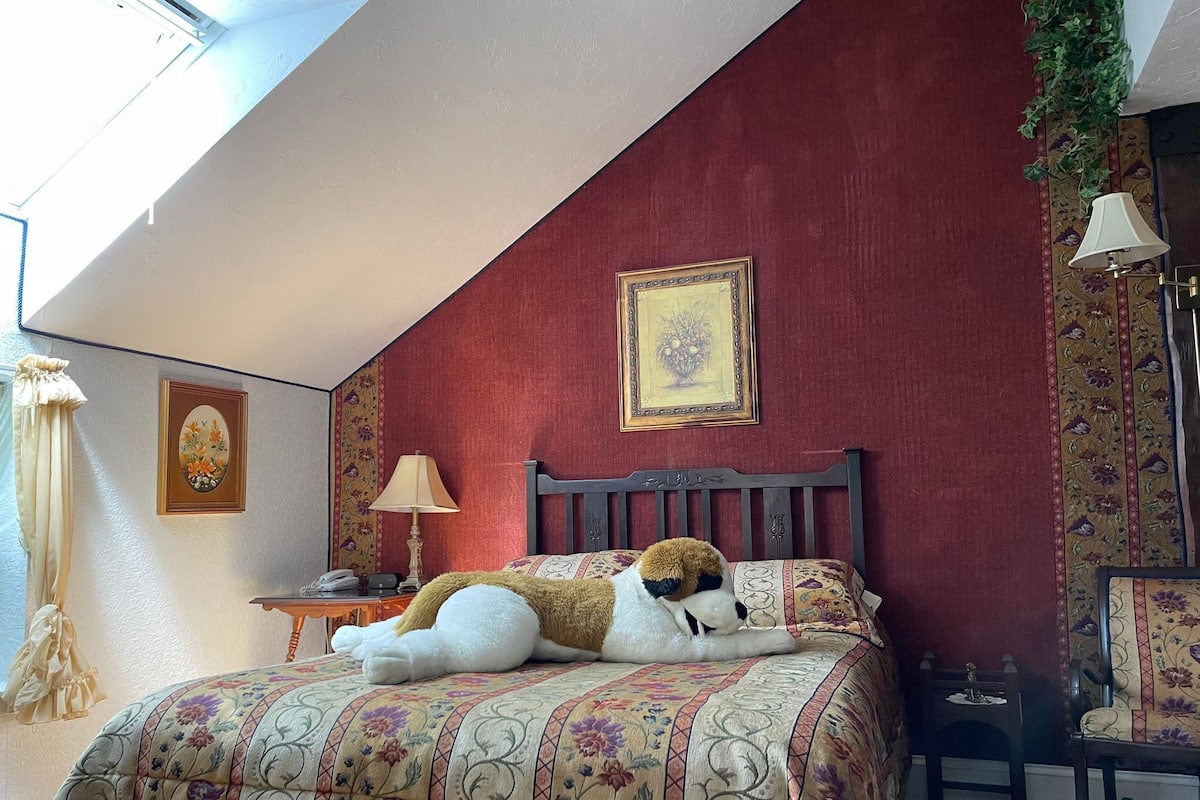 Un dormitorio con cama, mesita de noche, lámpara, silla y ventana con cortinas.